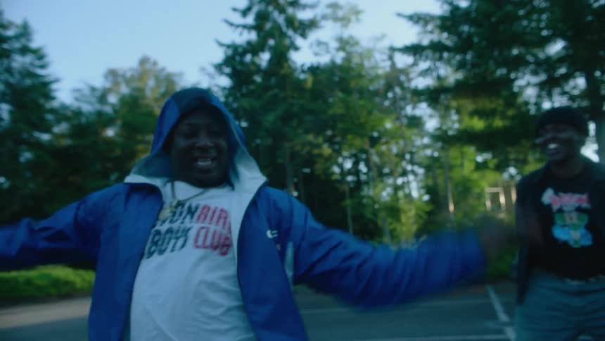 Three dancers wearing hats black blue jackets shorts and white sneakers dance next to black car in car park