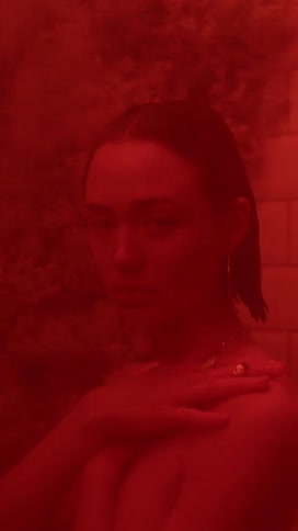 A woman stands in a room illuminated with red light with her arms crossed in front of her and her hands on her shoulders