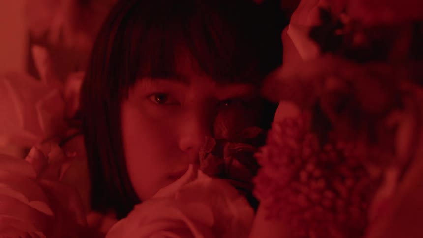 A woman poses in a wall of flowers in a room with red lighting