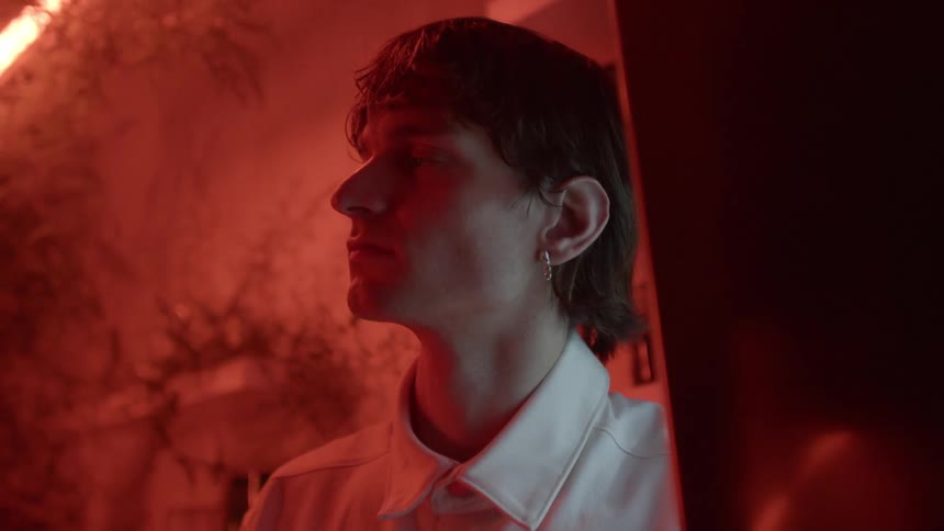 A man is standing in a room filled with plants and there is a light overhead and a red glow in the room