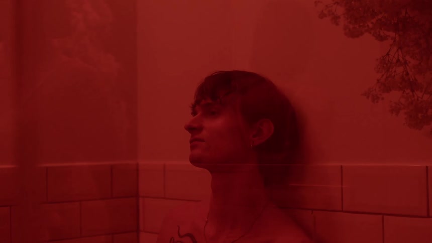 A young man leaning against a half tile wall bathed in a reddish glow