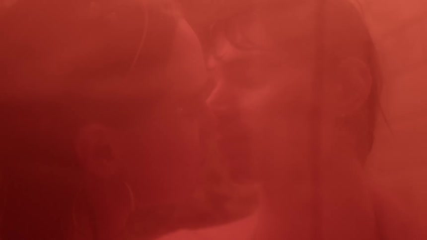 A bright red light shines upon a man and woman as they kiss
