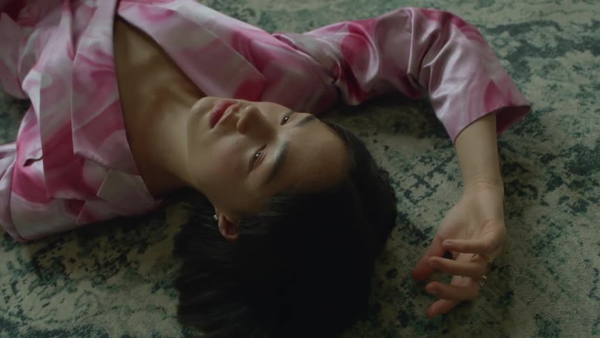 A young woman is lying on a rug on the floor and her arm is over her head as she blinks her eyes