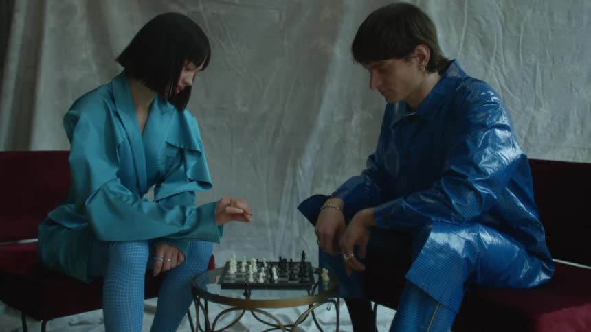 A man and a woman wearing blue raincoats are sitting down playing a game of chess
