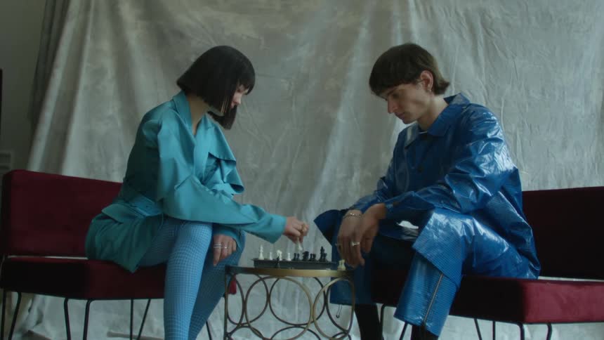 A woman and man play chess together at a small table indoors