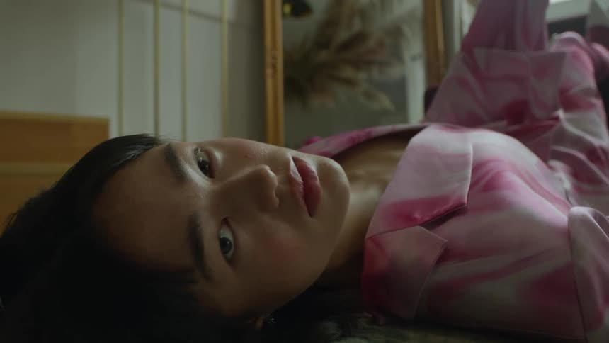 A young woman is lying still on the floor with her eyes open and she appears to be dead