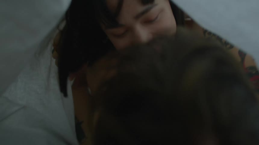 Man and woman cuddle under covers on bed