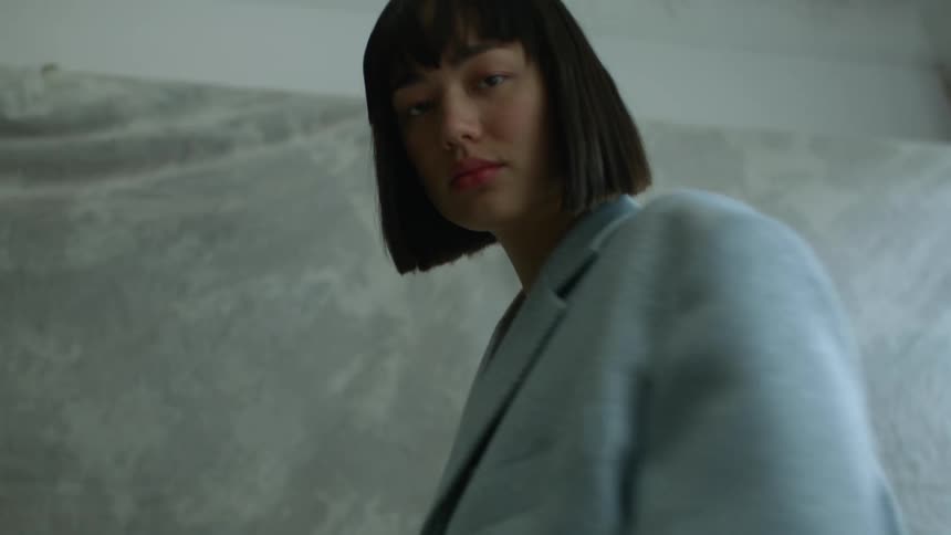 A model poses in a jacket while looking into the camera as she stands indoors during the day