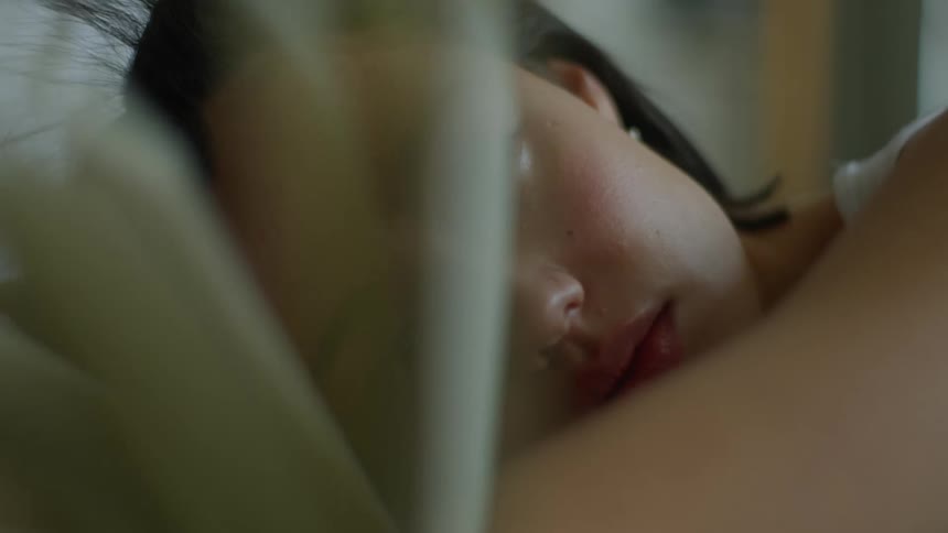 A woman is lying in bed with a book in front of her face and a fan is blowing the pages