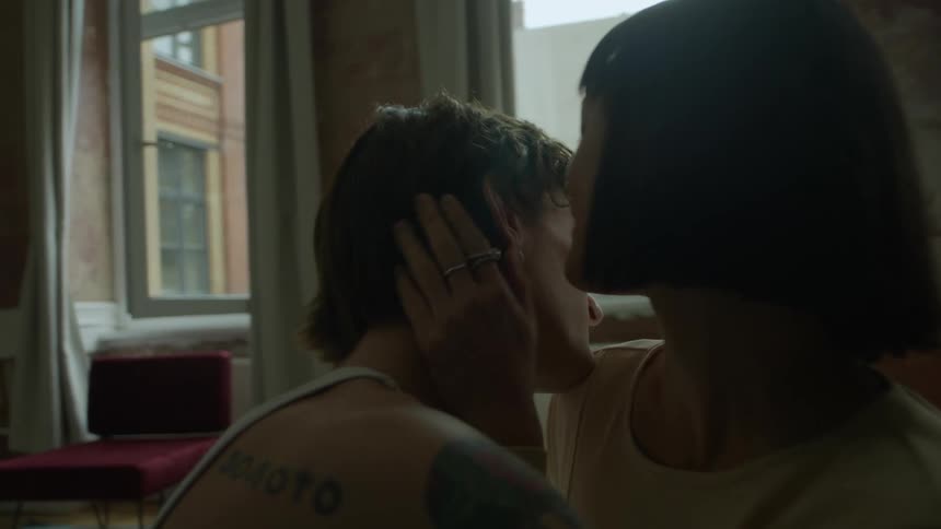 A woman pulls a man close and whispers into his ear while he embraces her indoors during the day