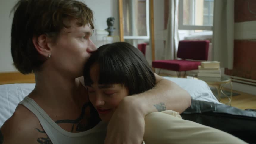 A man pulls his girlfriend in for a hug and kisses the top of her head