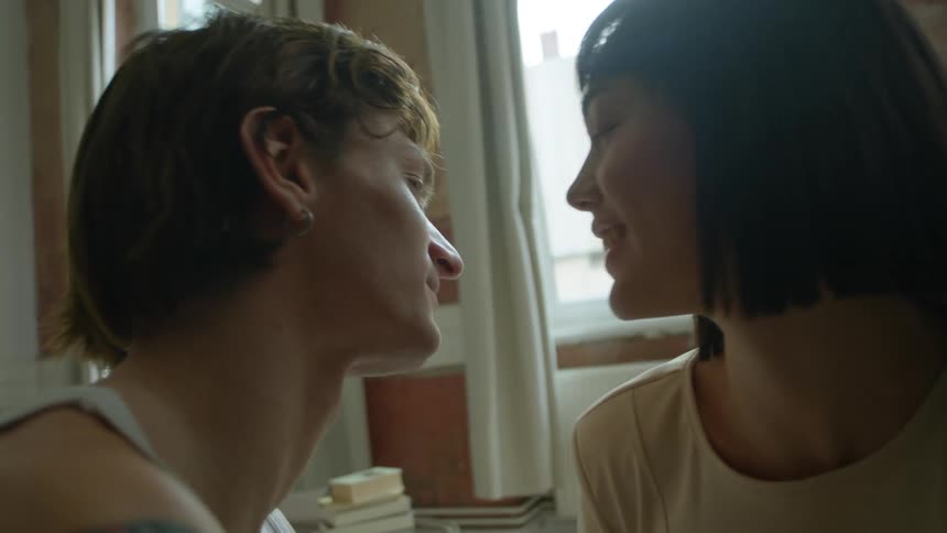 Couple sit close together near window smiling at each other