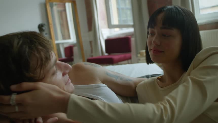 A woman brushes a mans hair in bed