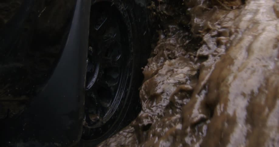 An automobile tire travels through a water puddle and splashes water into the air