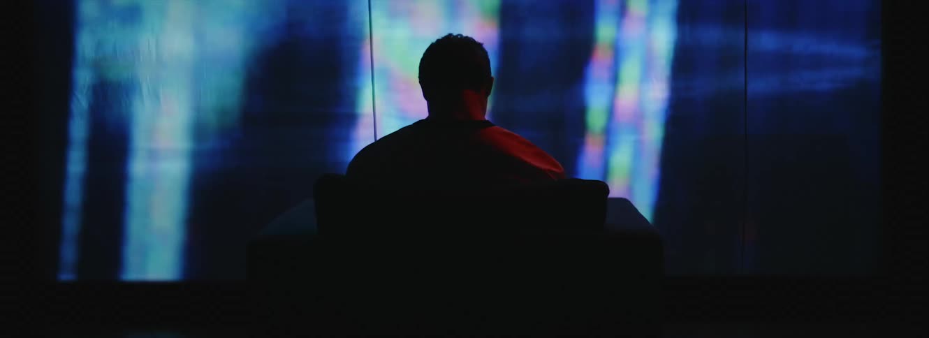 A man sits in a chair in front of a screen playing static