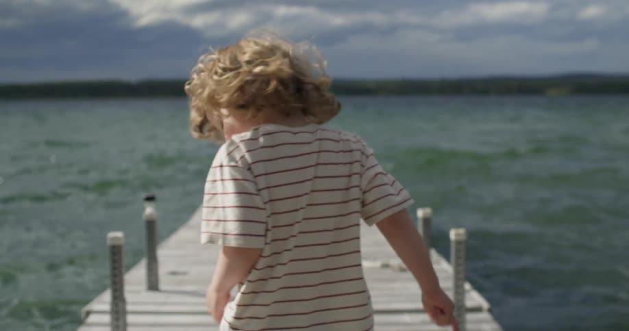 Blonde boy with striped shirt walks along the pier