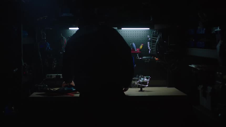 A man walks into a garage with tools on the wall and sets tools on a table