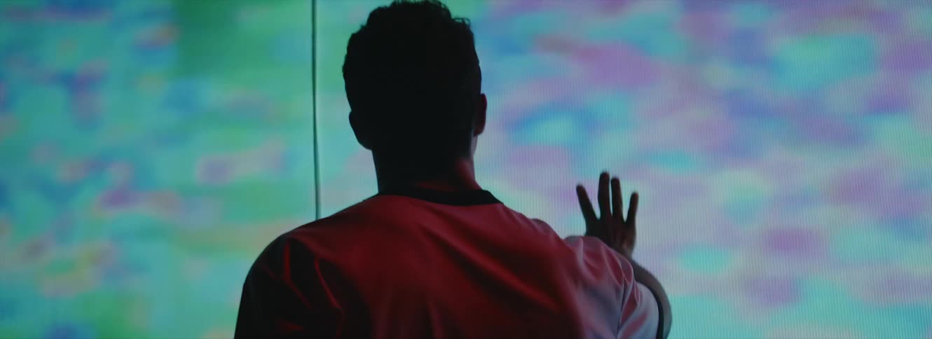 Man with white t shirt puts hand on large screen and looks around