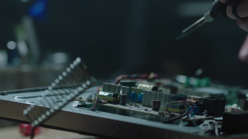 A man picks up a soldering tool and uses it on a circuit board