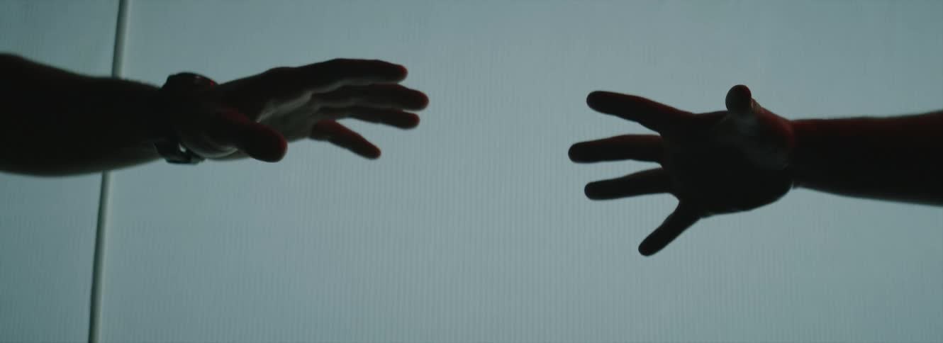 A man and woman stretch their arms and fingers while reaching for each other in front of a projector screen