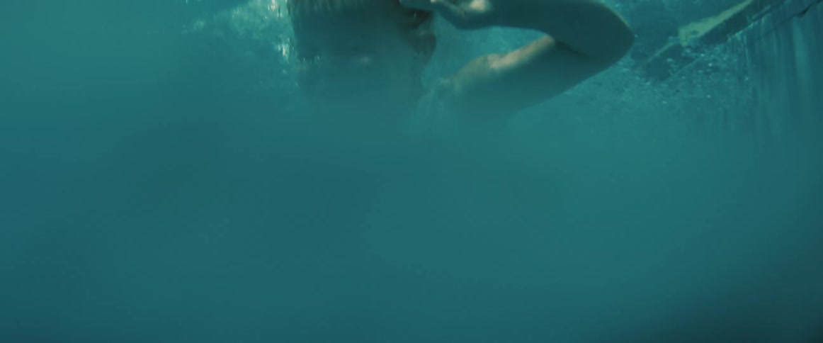 A little girl is at the edge of a swimming pool as she jumps in water splashes and she swims in the water