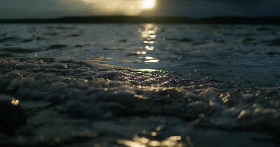 Sunset sunlight reflects over the ripples on the water gently crashing on the shore