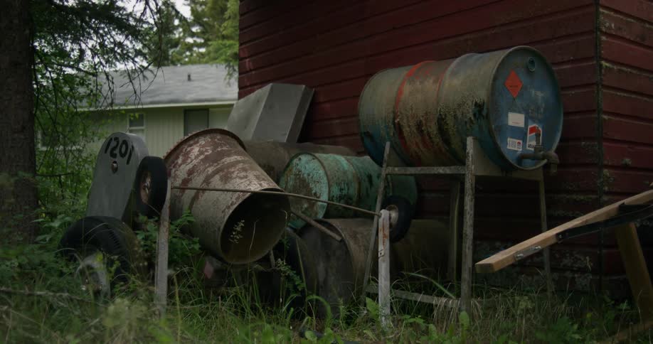 Piled up rusted metal barrels near a red brick wall on the backyard