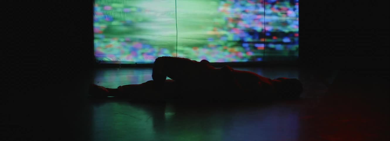 Man lying down on ground is silhouetted against the large screen