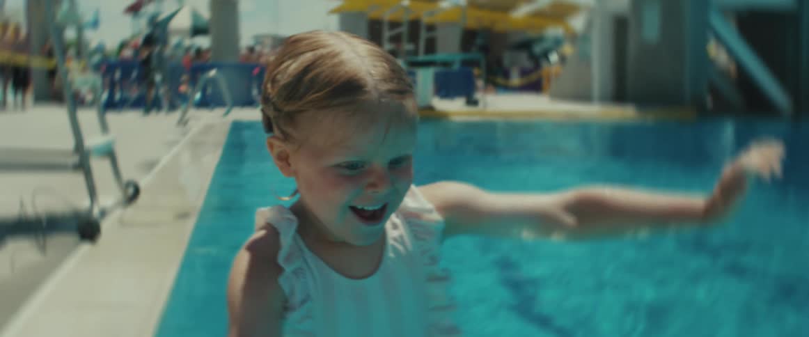 Happy smiling little girl wearing a cute swimsuit jumps into a public pool