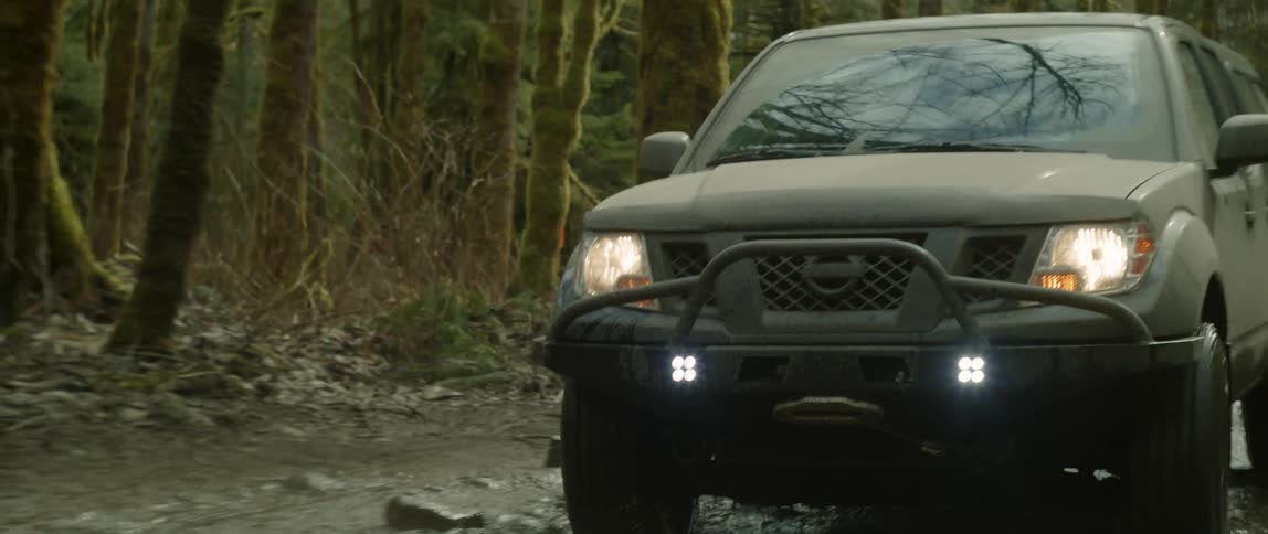 A truck traveling on a muddy dirt road splashes in and out of pot holes and puddles