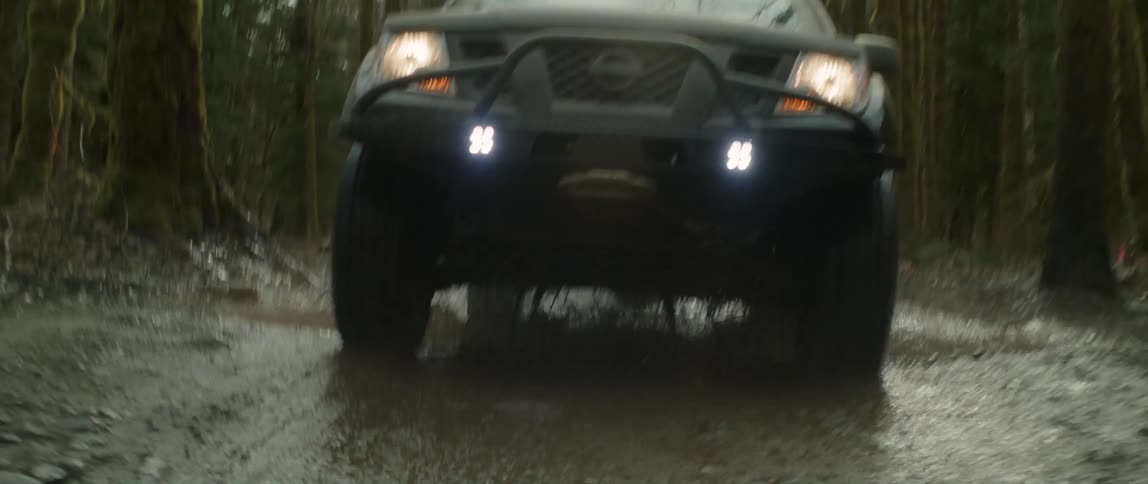 A sport utility vehicle drives through a puddle in the woods