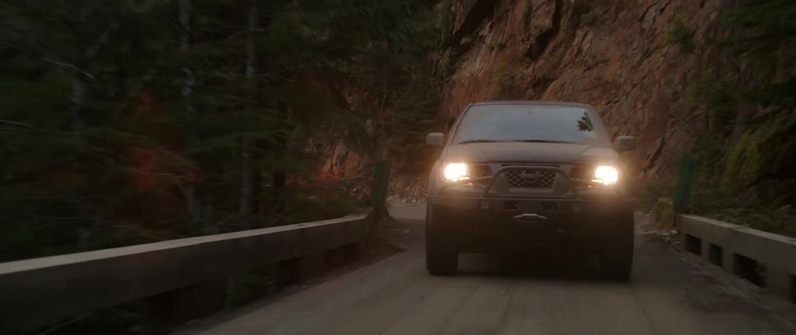 Vehicle with itsheadlights on drives through wilderness and crosses a bridge