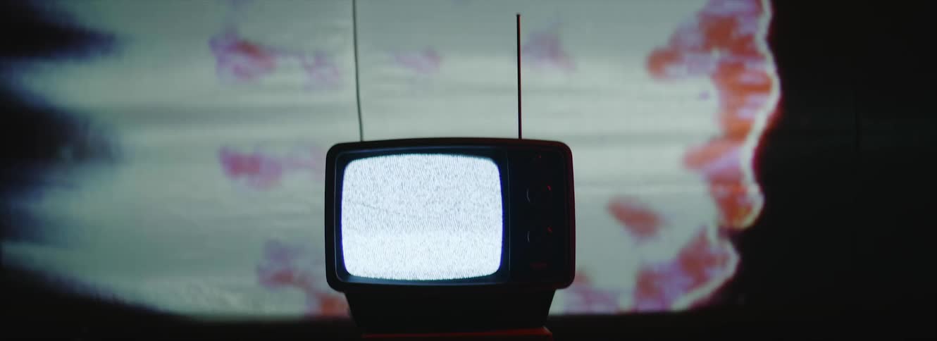 Static plays on the screen of a portable television as an unstable shape of light moves behind it