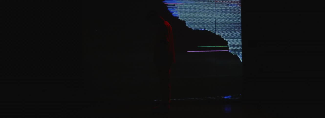 The silhouette of a man can be seen as he stands in front of a large screen displaying static and distortion