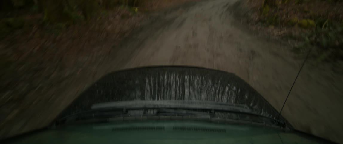 Car driving through mud patches on a wet dirt road