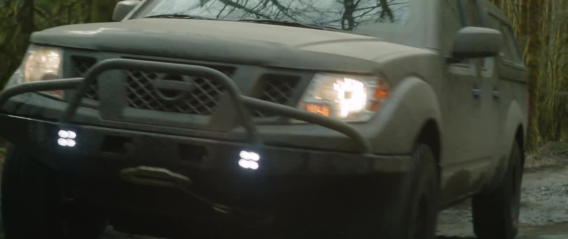 An automobile with the headlights on is bouncing up and down as it travels on a road through the woods