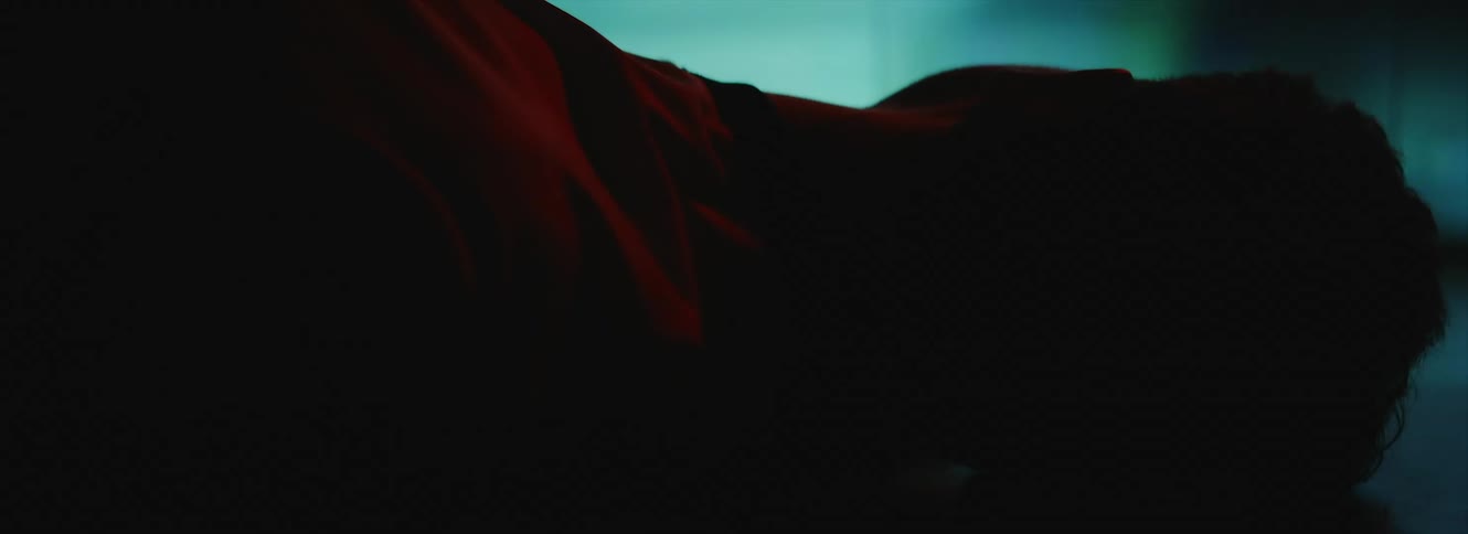 Man with white t shirt lying on ground is silhouetted against the large screen in dark room
