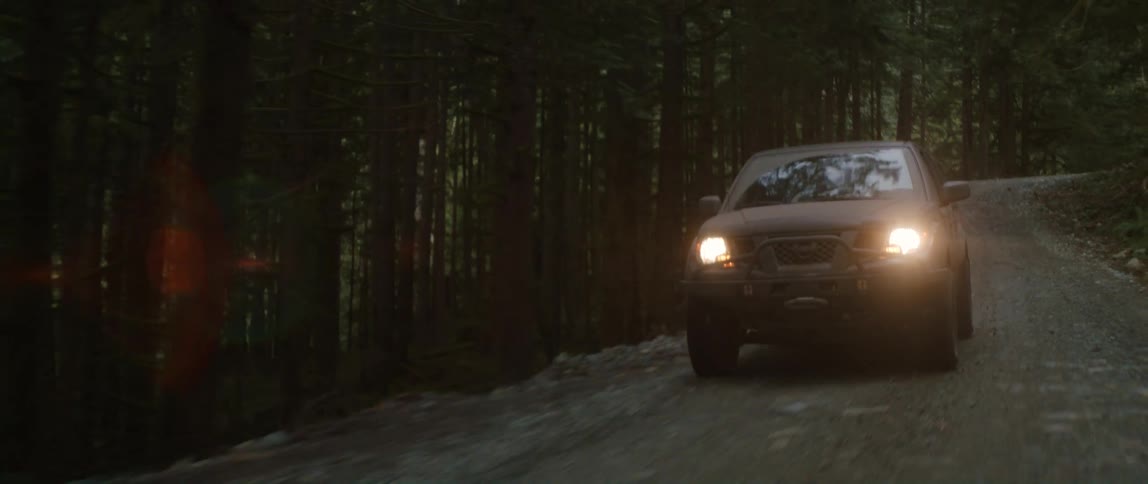 Vehicle with the headlights on drives along dirt road through forest on slope