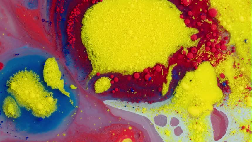 Blobs and clumps of colorful paint floating on the surface shift when yellow is squirted in