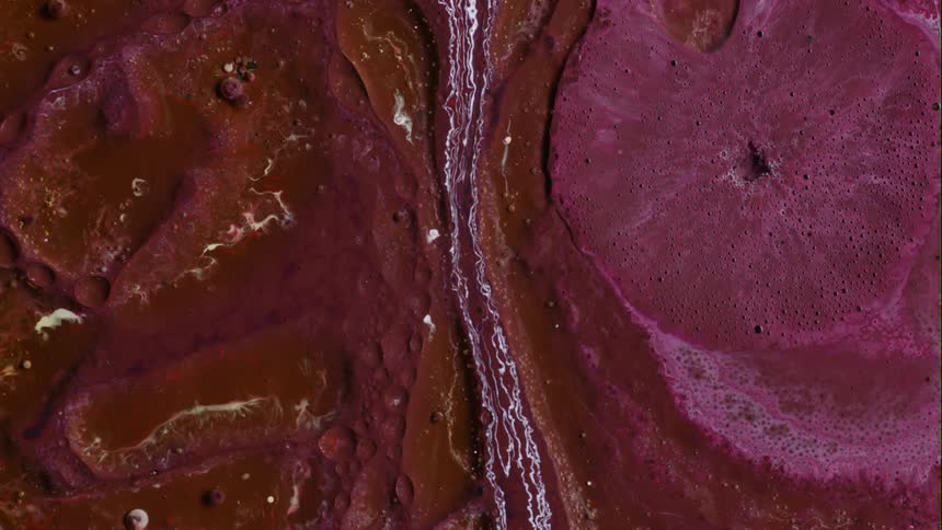 Close up of chaotic red and pink liquid ink bubbling and expanding