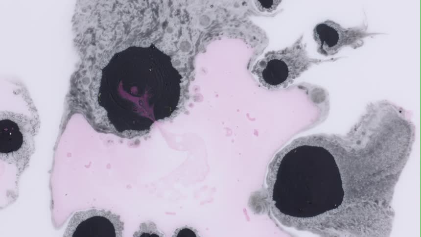 Pink tinted liquid expands in mixture near dark spots surrounded by gray