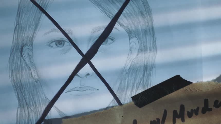 An x is marked across a drawing of a woman with a handwritten note taped on it