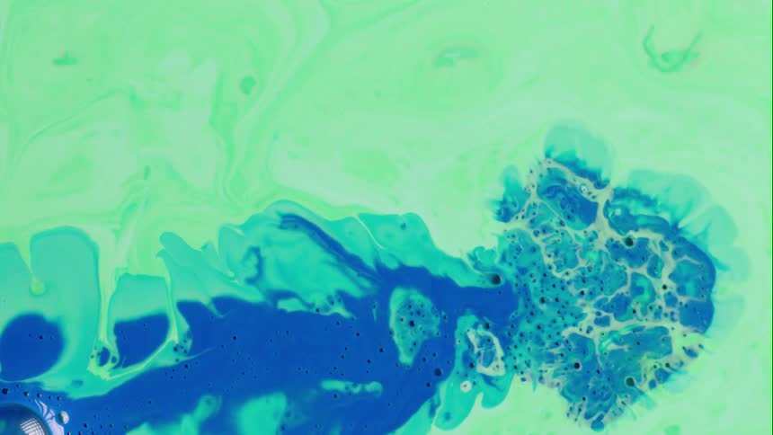 Blue liquid is splashed onto light green and the colors blend as they move