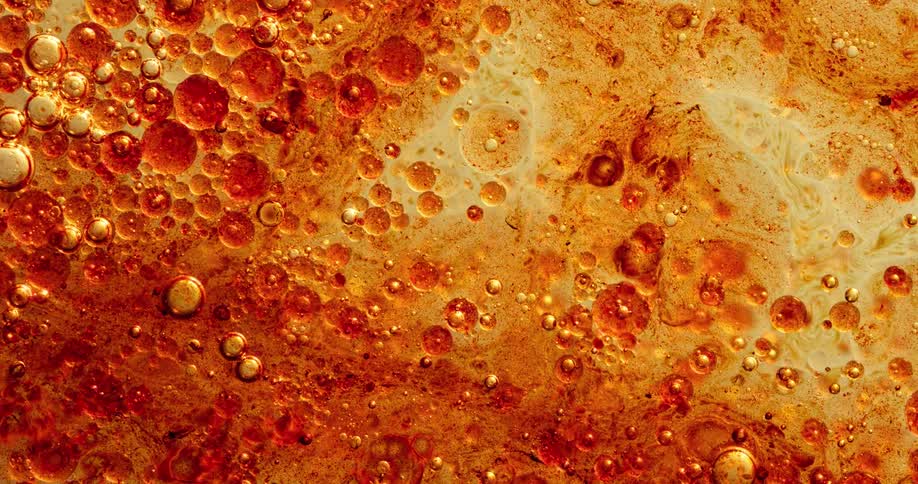 A yellow and orange organic substance boils and bubbles pop and turn darker as spheres float across the surface