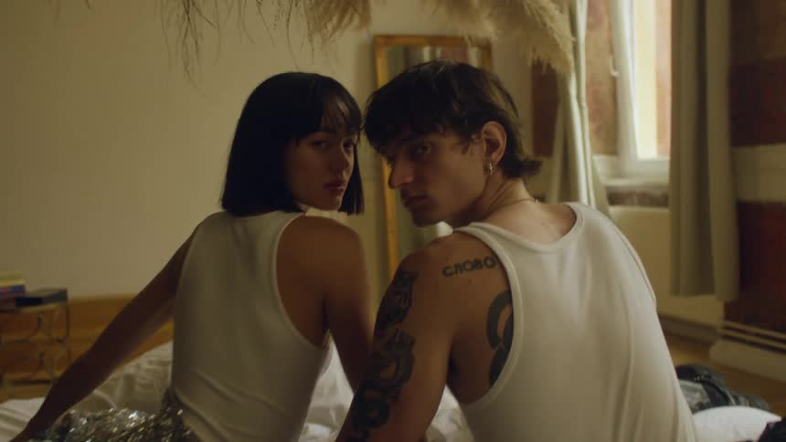 A couple turn and pose in matching tank tops while sitting in bed