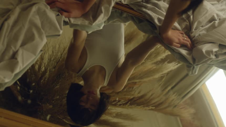 Woman leans over mirror with closed eyes as breeze blows hair around