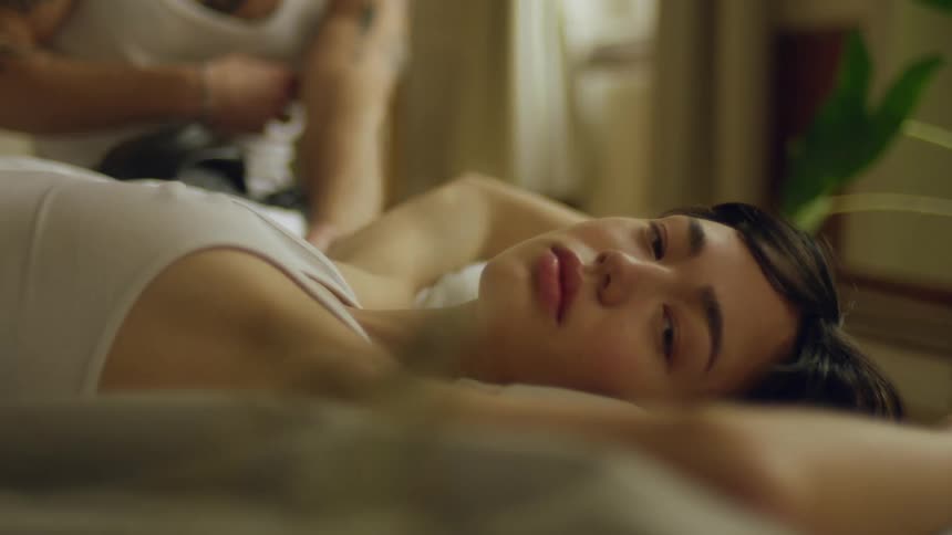 A teenage boy lies in bed as another man sits by the bed