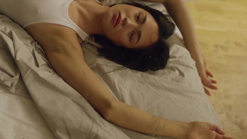 Woman lies on bed as tendrils are blown across her arm