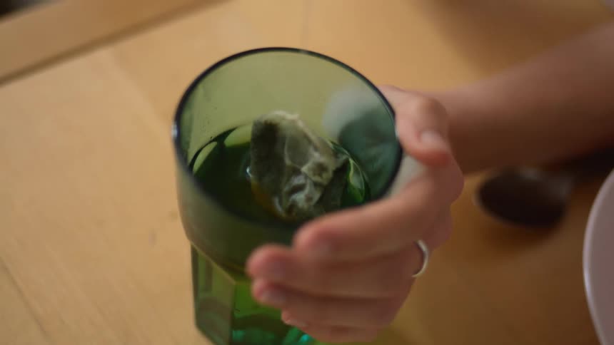 A woman steeps a tea bag in a glass