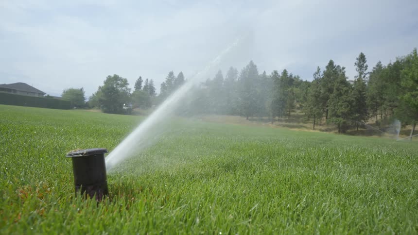 Sprinkler sprays water onto green grass in the countryside